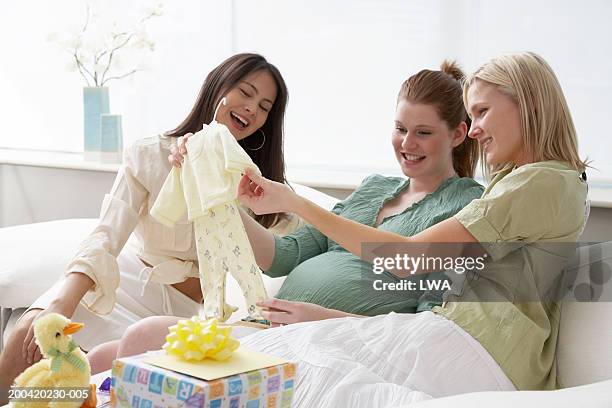two friends with pregnant woman looking at baby's clothing, smiling - chá de bebé imagens e fotografias de stock