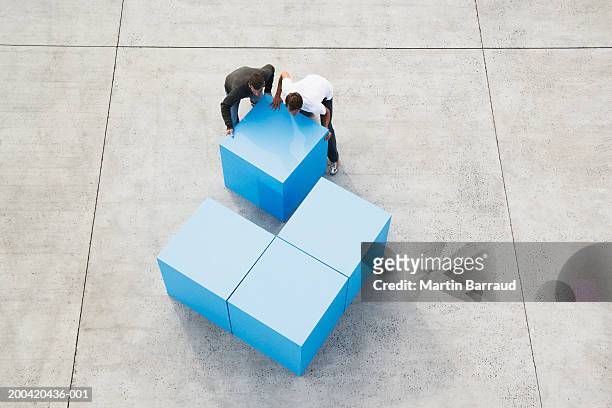 two men moving large blue block, elevated view - baustein stock-fotos und bilder