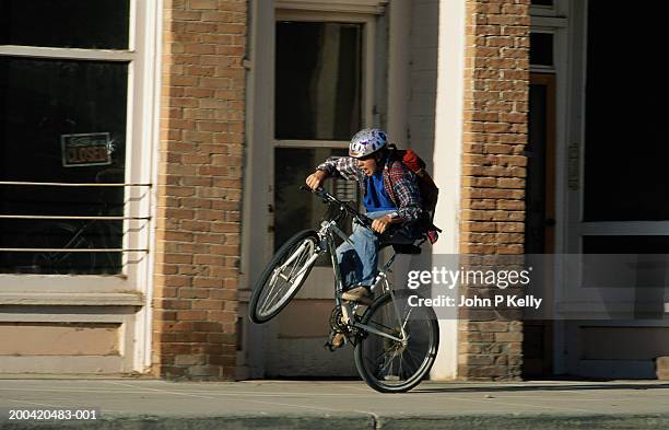 teenage boy (13-15) doing wheelie on town street - wheelie stock pictures, royalty-free photos & images