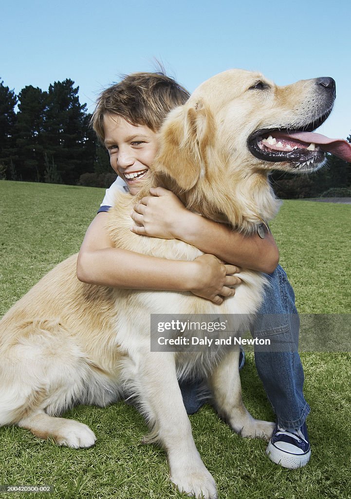 Boy (8-10) hugging golden retriever, smiling, portrait