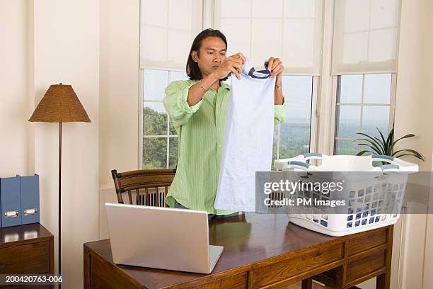 man folding laundry with laptop on table - geplooid stockfoto's en -beelden