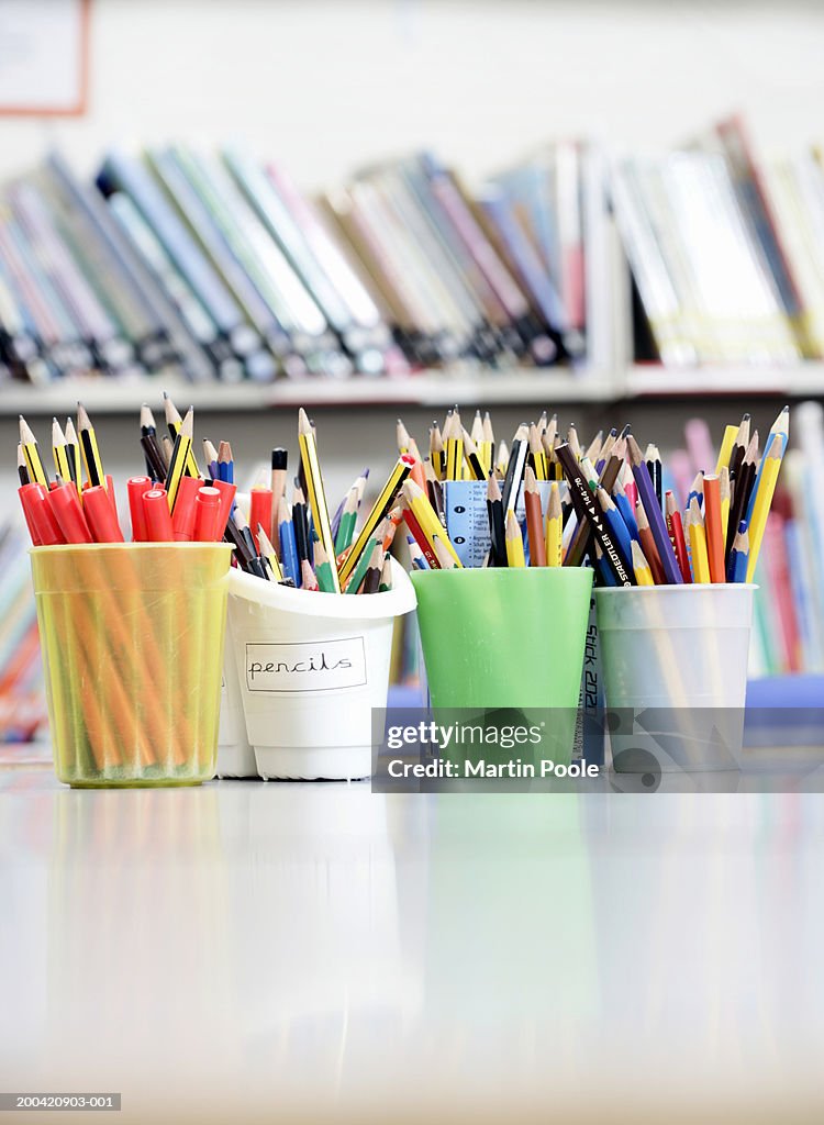 Row of pencil pots on desk in classroom