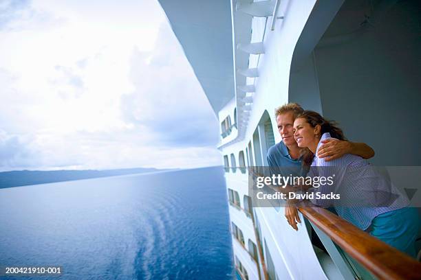 couple leaning on rail of cruise ship, looking at ocean - kreuzfahrt stock-fotos und bilder