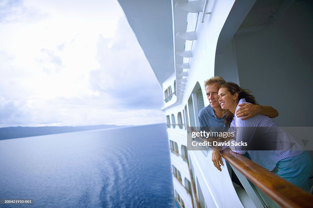 Couple leaning on rail of cruise ship, looking at ocean