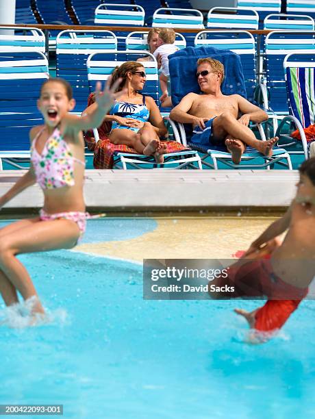 children (10-12) jumping into pool, people in background - sunbed stock pictures, royalty-free photos & images