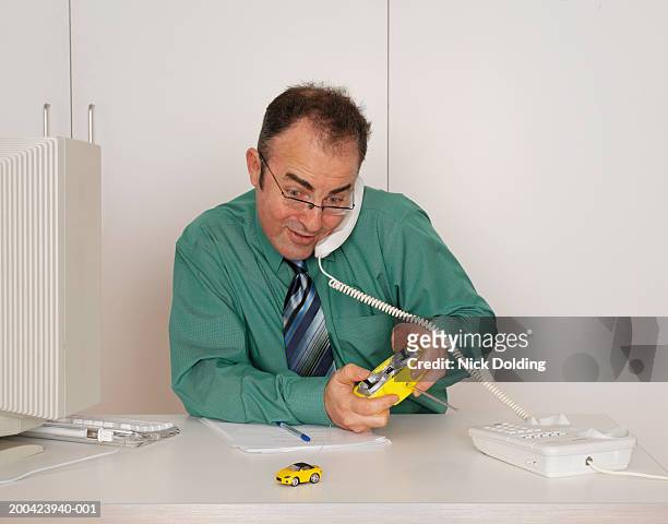 business man sitting at desk playing with remote control car - remote control car games stockfoto's en -beelden