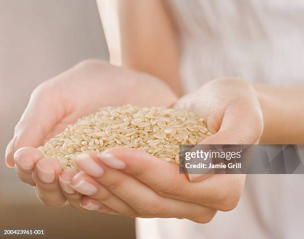 woman holding handful of brown rice, close-up - naturreis stock-fotos und bilder