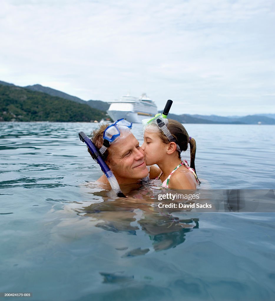 Father with daughter (10-12) in water, girl kissing father
