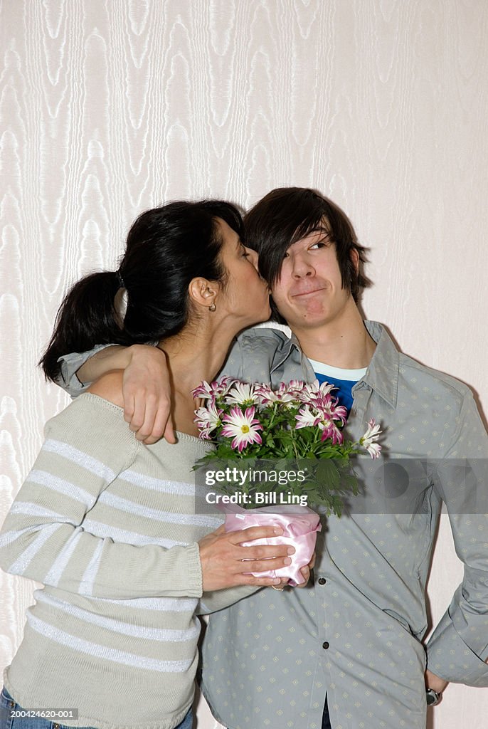 Mother holding gift, kissing teenage son (13-15) on cheek