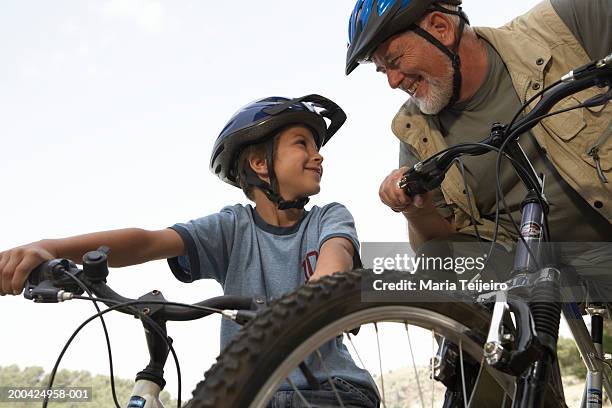 boy (5-7) and grandfather on mountain bikes, smiling, low angle view - training wheels stock-fotos und bilder