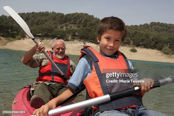 boy (5-7) and grandfather canoeing on lake, smiling, portrait - family red canoe stock pictures, royalty-free photos & images