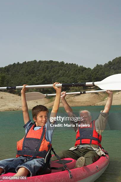 boy (5-7) and grandfather in canoe, holding up oars, smiling, portrait - family red canoe stock pictures, royalty-free photos & images