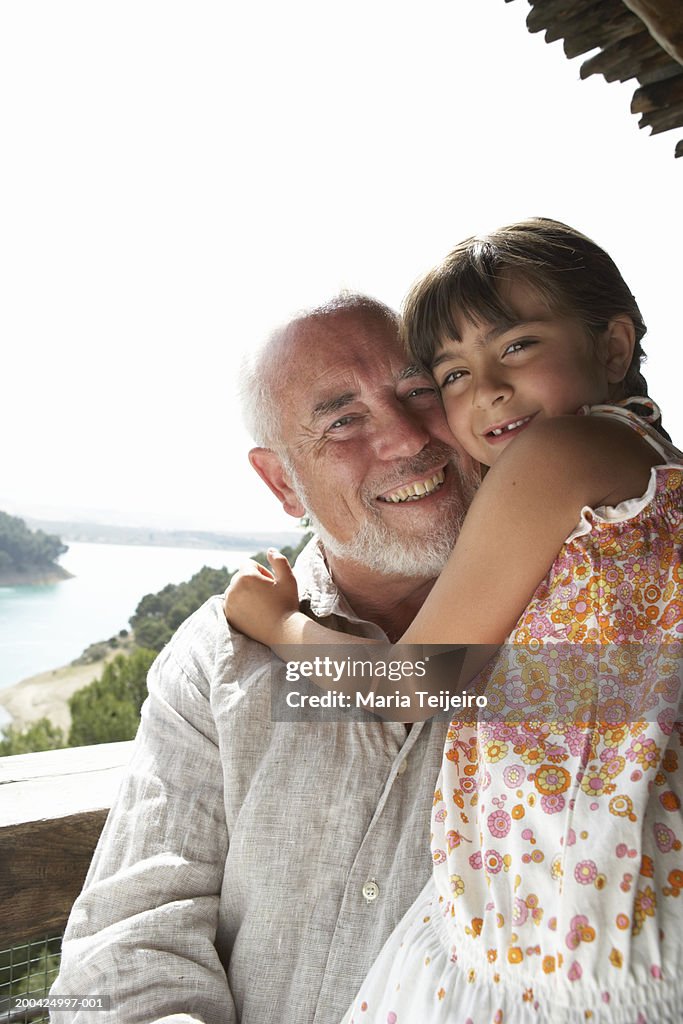 Girl (4-6) embracing grandfather, smiling, portrait