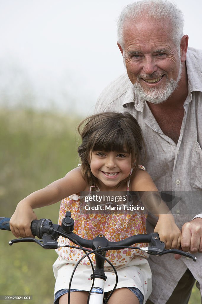 Grandfather supporting girl (4-6) on bike, smiling, portrait