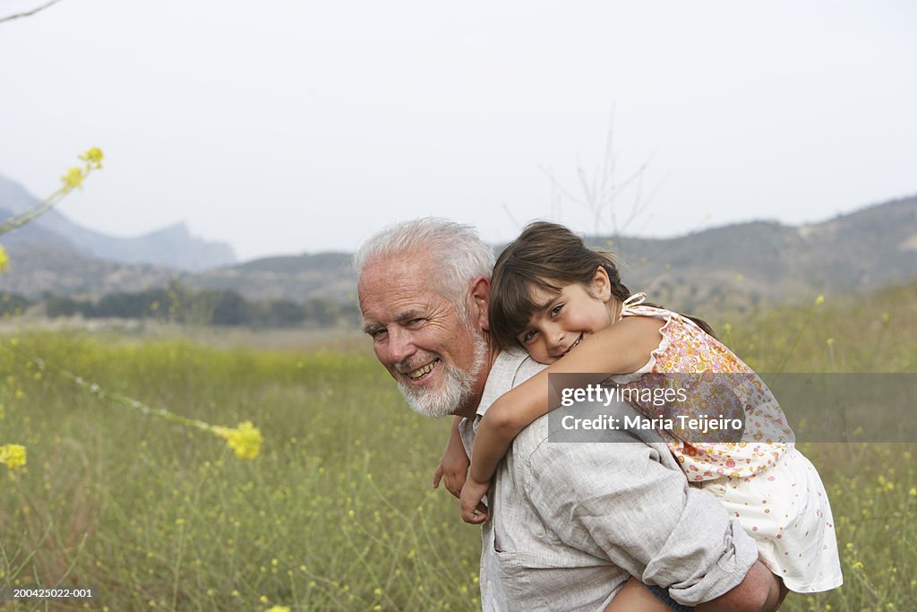 Grandfather giving girl (4-6) piggyback, smiling, portrait, side view