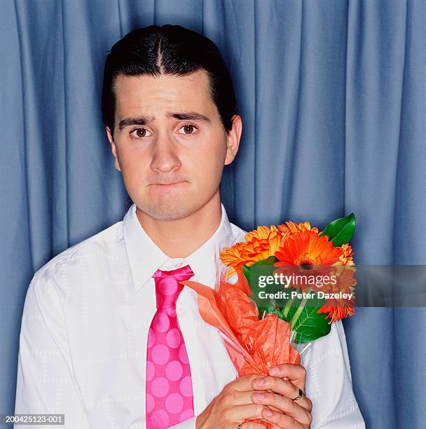 young man holding bunch of gerberas, biting bottom lip, portrait - arrossire foto e immagini stock