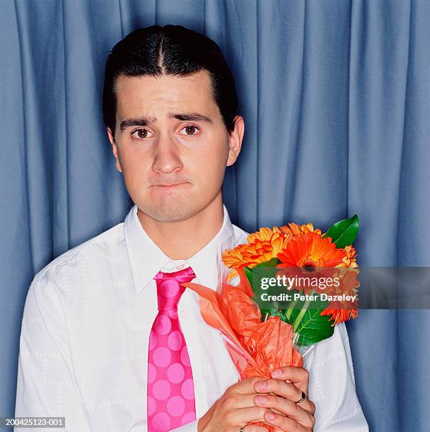 young man holding bunch of gerberas, biting bottom lip, portrait - 唇を噛む ストックフォトと画像