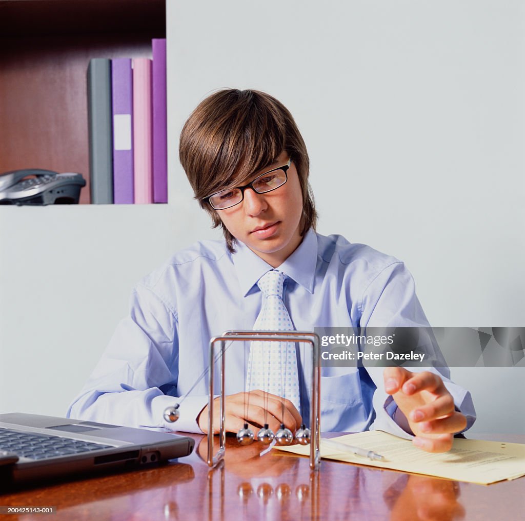 Teenage boy (14-16) in shirt and tie swinging ball on Newton's Cradle