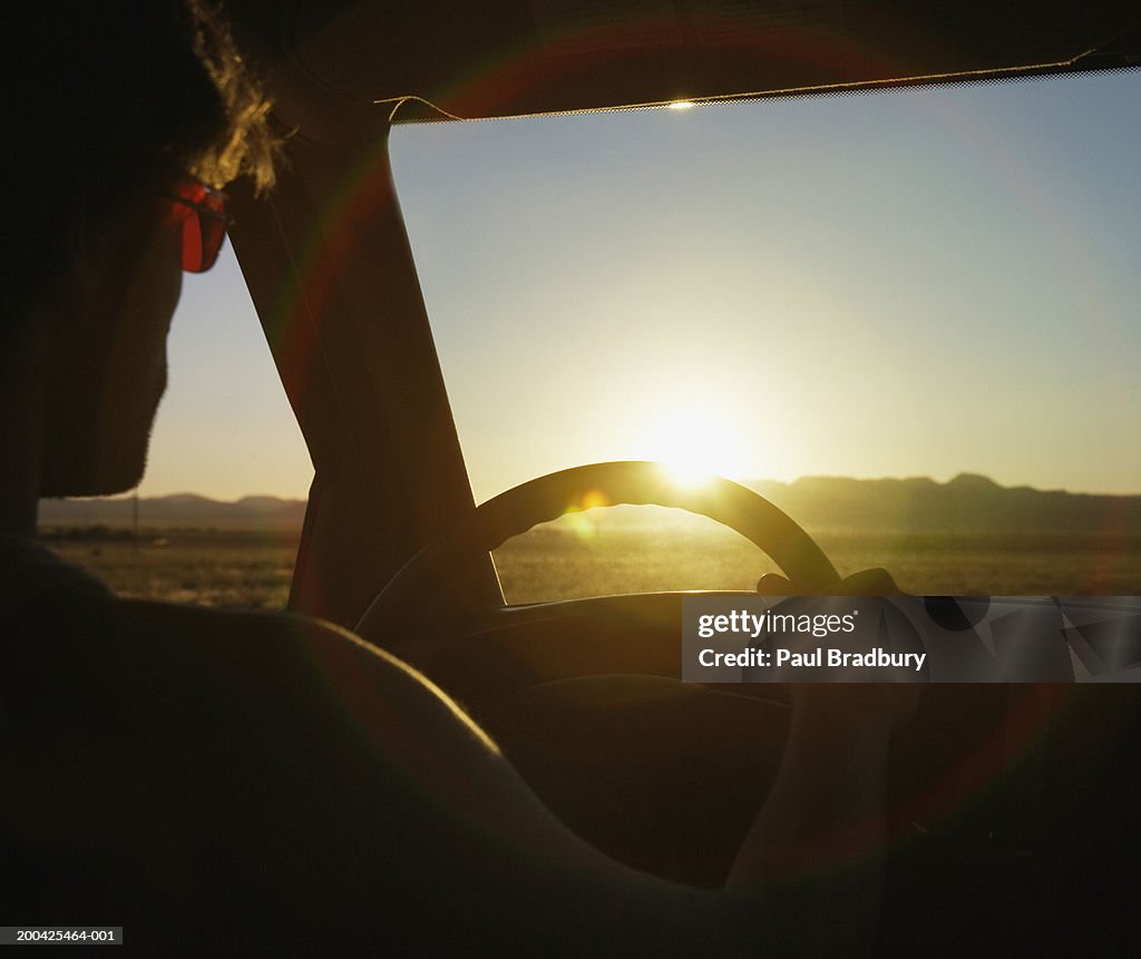 USA, Nevada, man driving in desert landscape, close-up, sunset