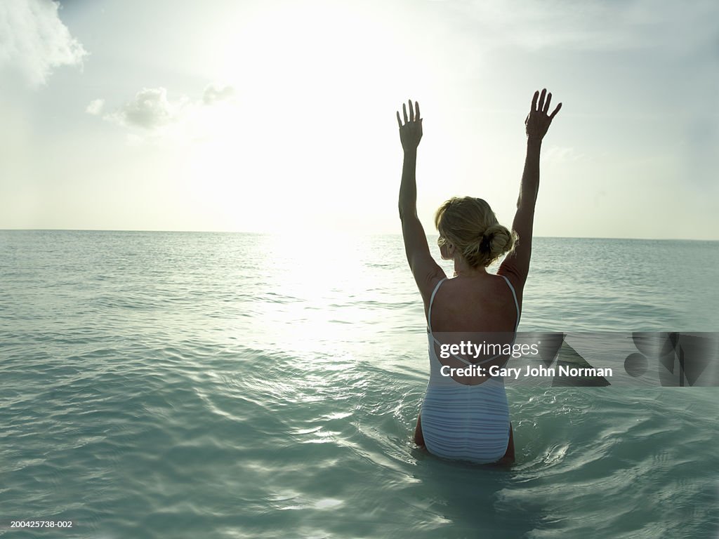 Woman lifting arms in ocean, rear view