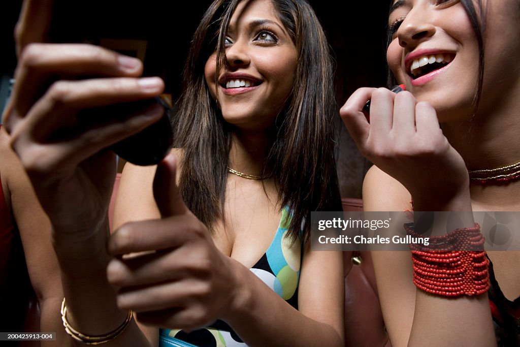 Two young women sitting, applying make-up