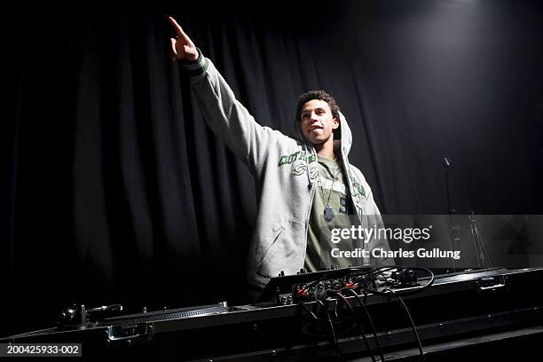 young man behind record table, pointing in air - dj de club fotografías e imágenes de stock