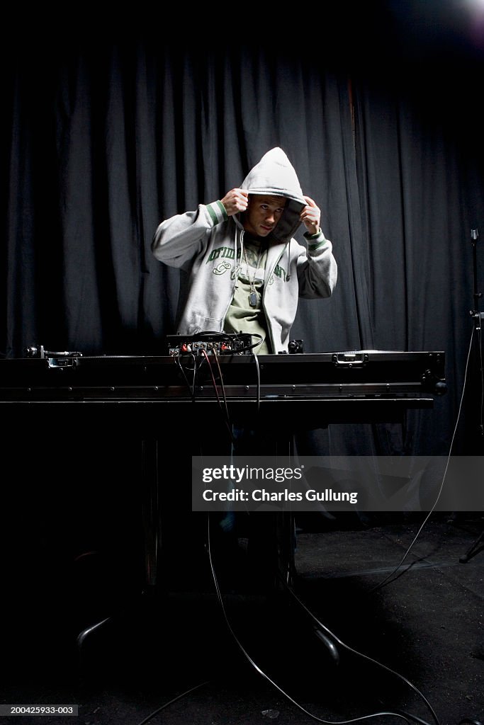 Young man behind record table, pulling hood over head