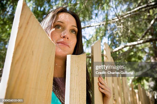 young woman looking over fence, low angle view - bad neighbor foto e immagini stock