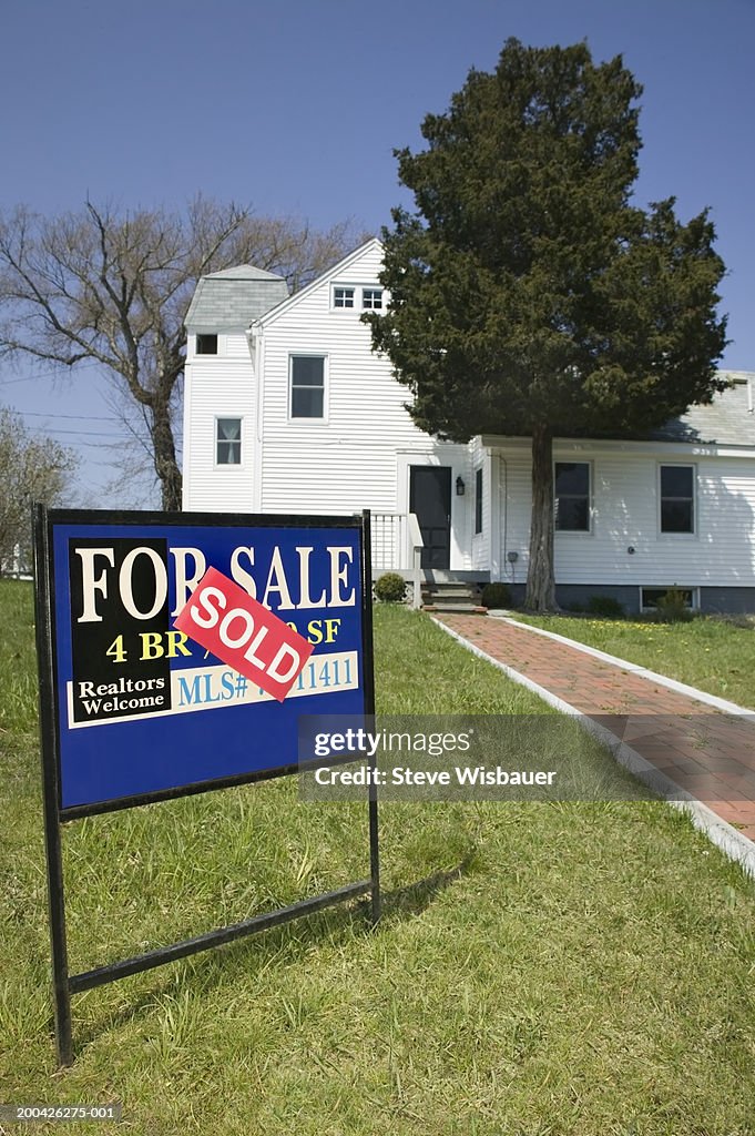 'For Sale' sign on lawn in front of house