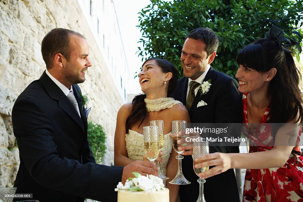Bride and groom toasting champagne glasses with friends, smiling