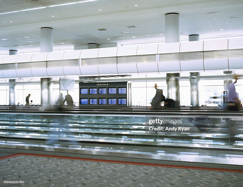 People walking on moving walkway in airport, side view (blurrd motion)