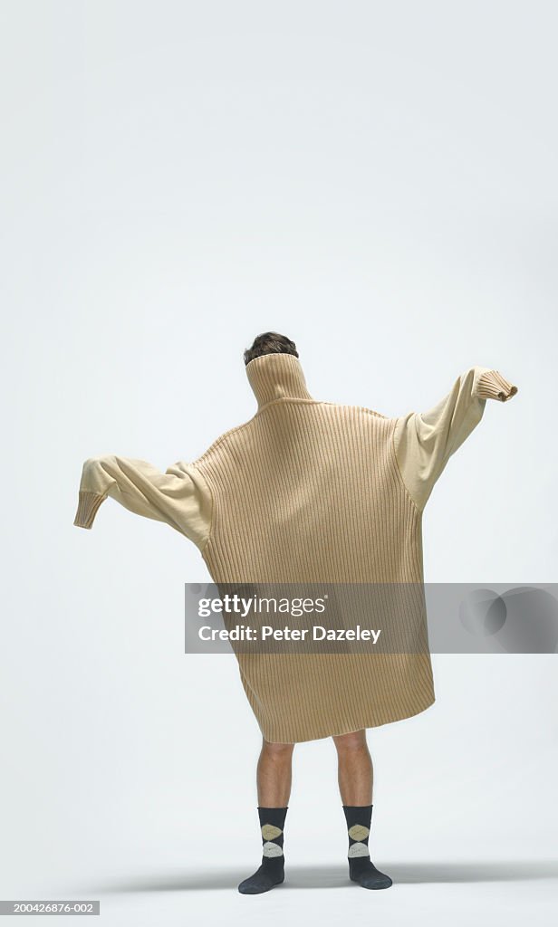 Young man wearing large jumper over head and body, arms outstretched