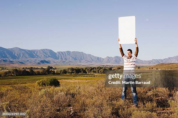 man standing in bush land holding blank whiteboard above head - hochhalten stock-fotos und bilder
