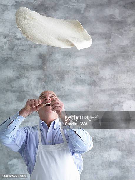 mature man in apron throwing pizza dough in air, close-up - pizza toss foto e immagini stock