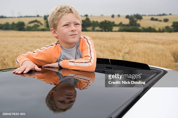 boy (8-9 years) looking out of open sunroof of car in countryside - 8 9 years stock-fotos und bilder