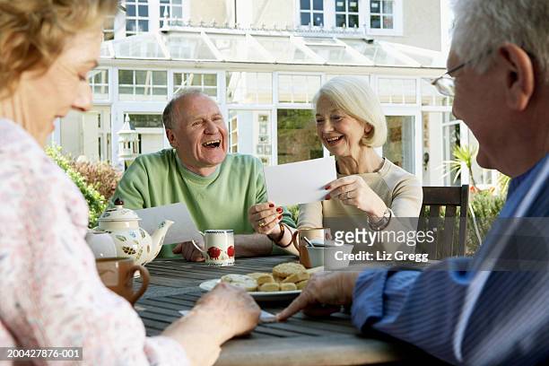 two senior couples looking at photographs around garden table, smiling - blue teapot stock pictures, royalty-free photos & images