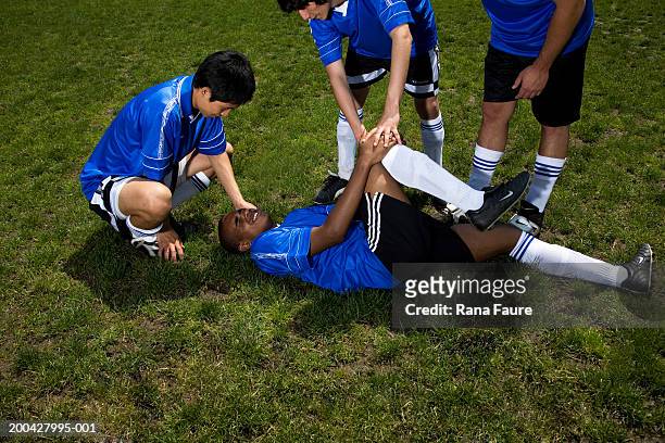 teenage male (16-20) soccer players helping injured teammate - injured football player stock pictures, royalty-free photos & images