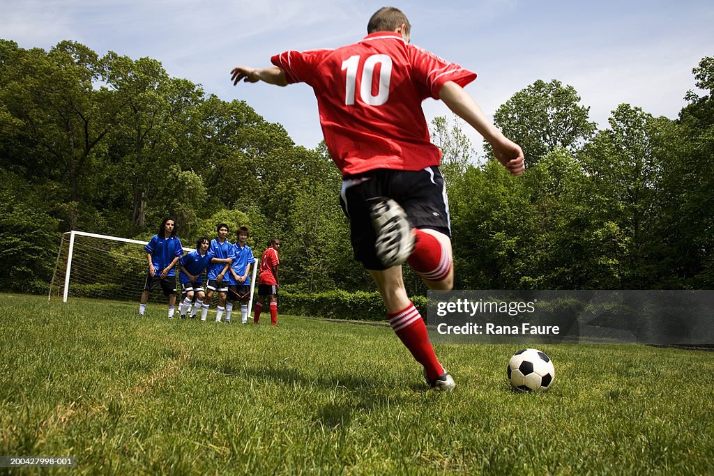 Teenage male (18-20) soccer player free kicking against opposing team
