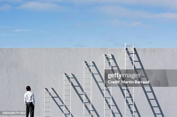 businessman looking at row of different sized ladders against wall - position stock pictures, royalty-free photos & images