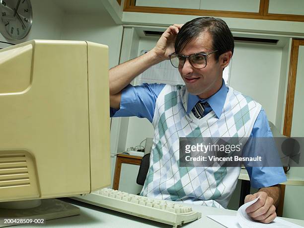 man working at office desk, looking at computer and scratching head - verwarring stockfoto's en -beelden
