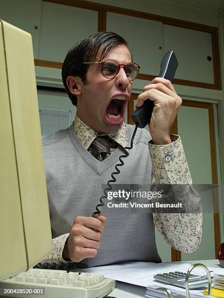 man sitting at office desk yelling into telephone receiver, close-up - close up phone on surface stock-fotos und bilder