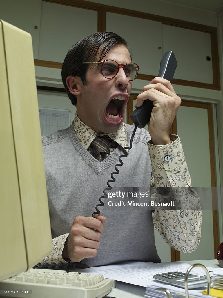 Man sitting at office desk yelling into telephone receiver, close-up