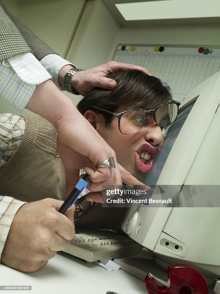 Manager pushing office worker's face against computer screen