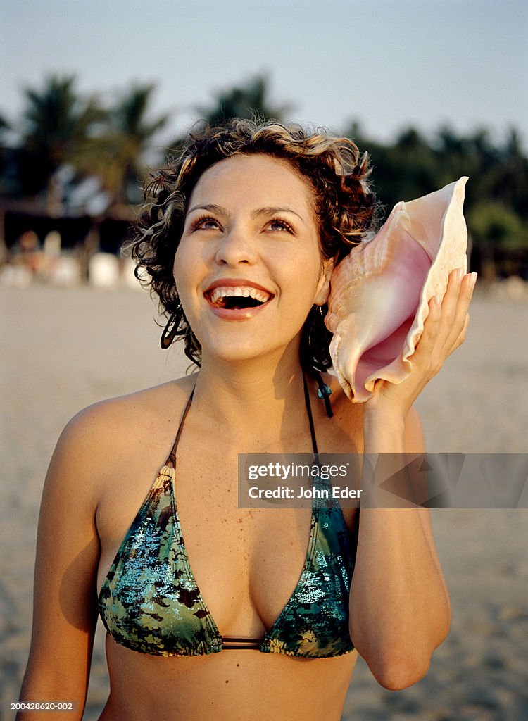 Young woman holding conch shell against ear