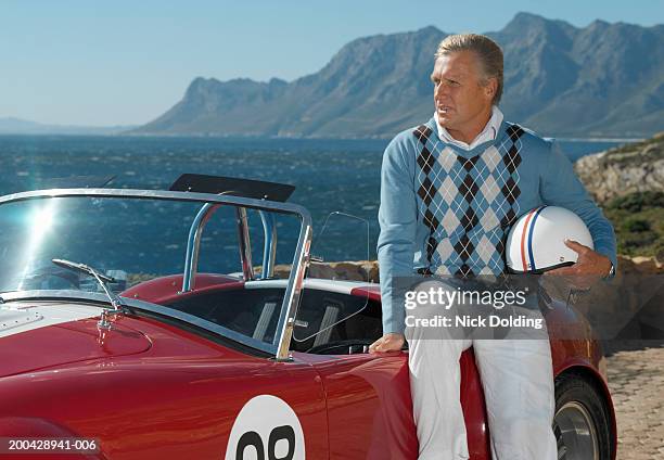 mature man holding helmet sitting on convertible racing car by coast - sports car top imagens e fotografias de stock