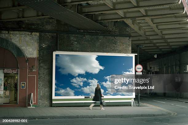 woman walking past billboard poster of cloudy sky on city street - sidewalk stock pictures, royalty-free photos & images