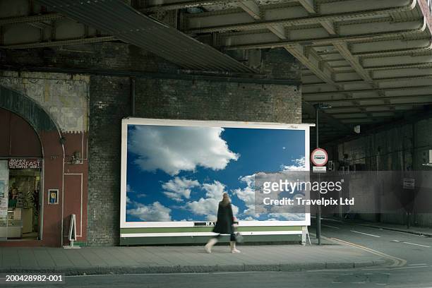 woman walking past billboard poster of cloudy sky on city street - advertising sign imagens e fotografias de stock