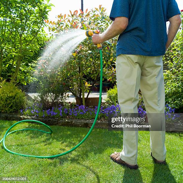 senior man watering garden with hose, rear view - garden hose foto e immagini stock