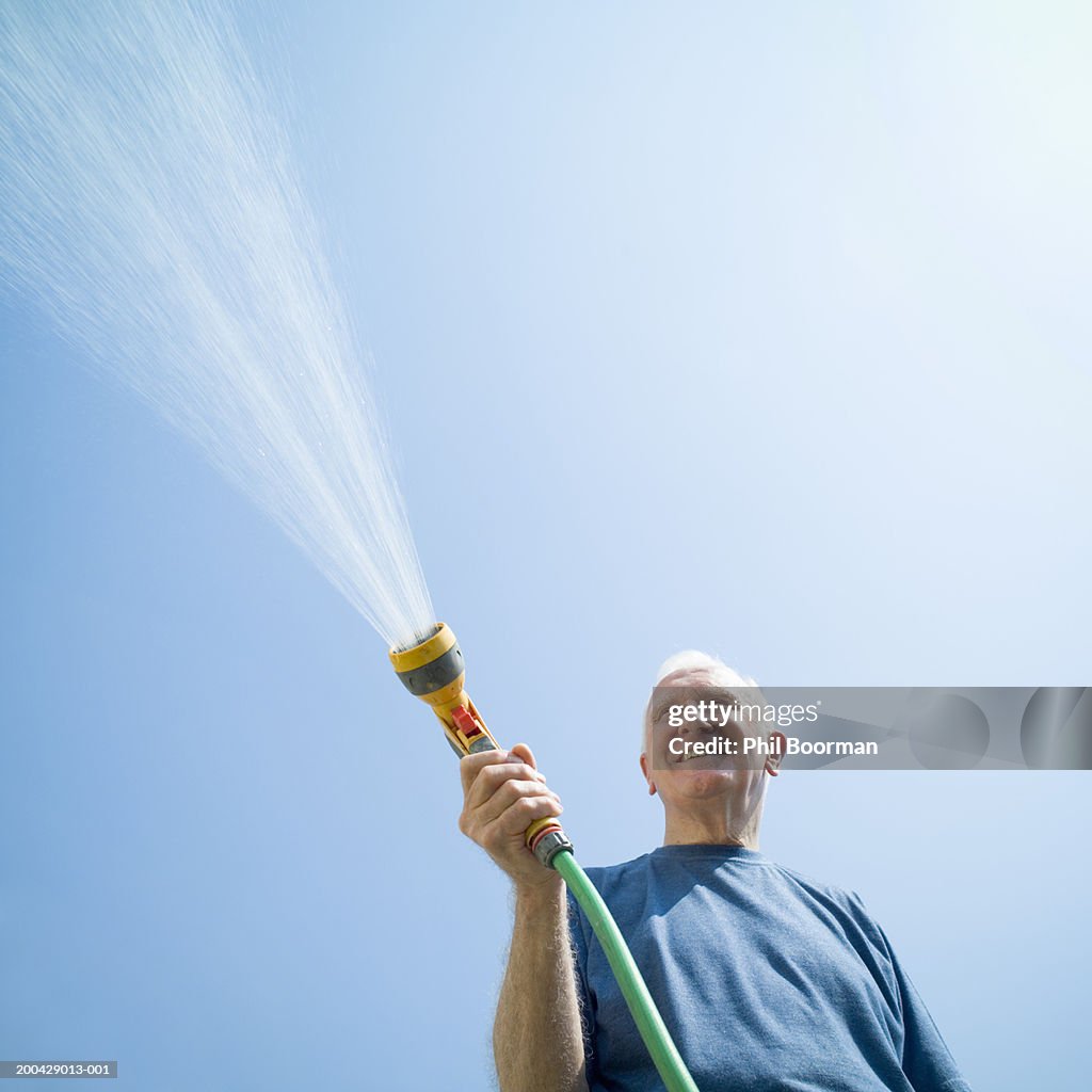 Senior man using garden hose, smiling, low angle view