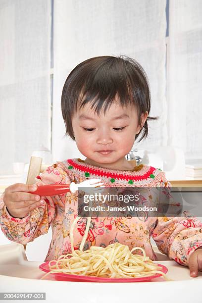 baby girl (18-24 months) in high chair eating spaghetti with fork - one baby girl only bildbanksfoton och bilder